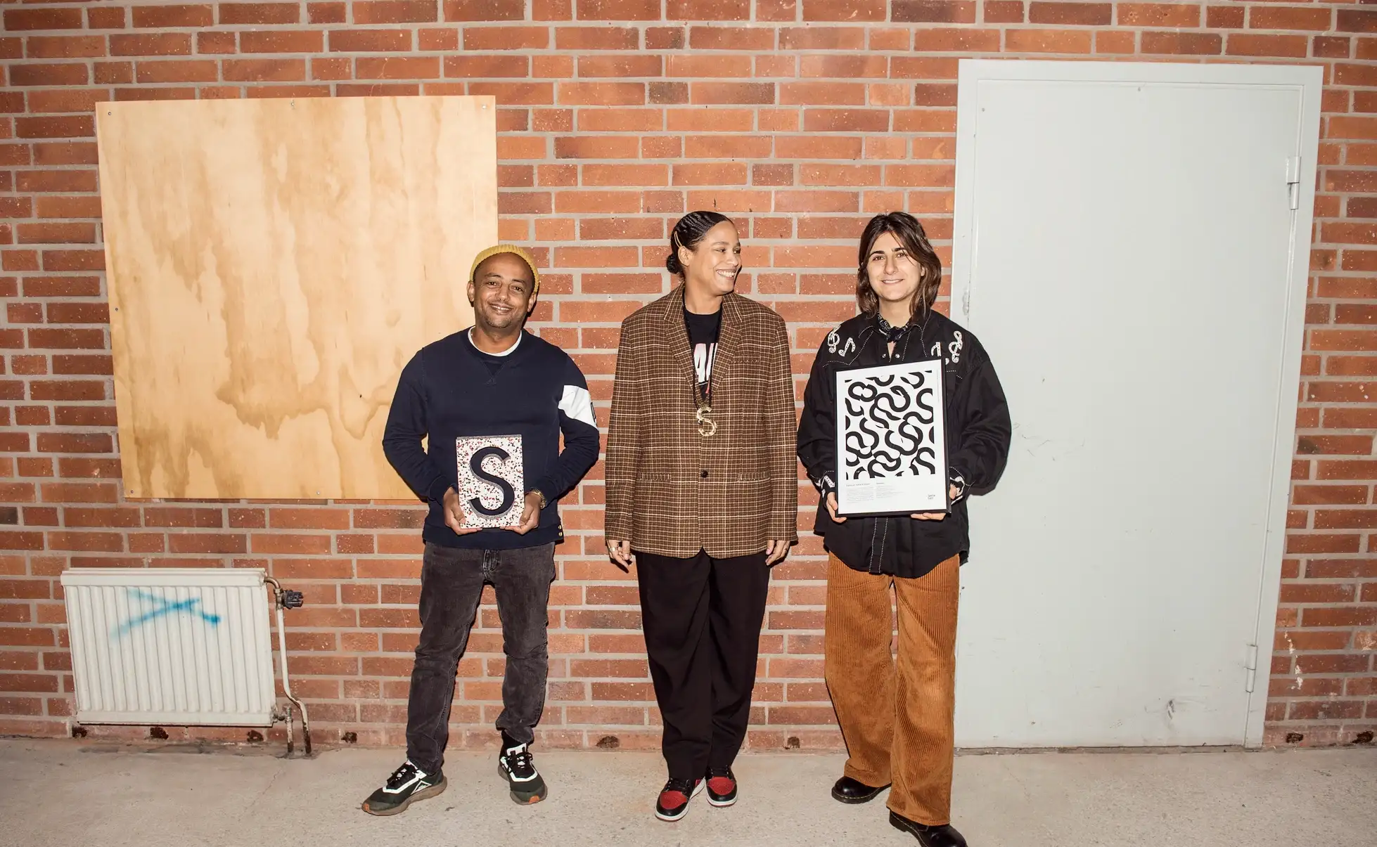 Afripedia team holding award prints in front of a brick wall
